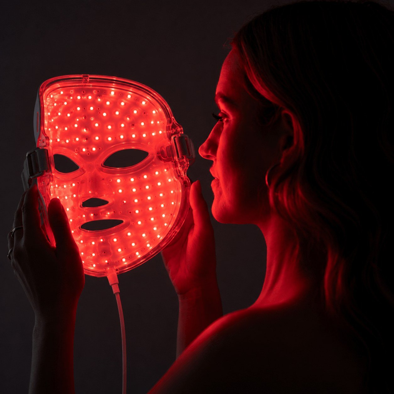 Woman holding a red-light LED therapy mask glowing during a session